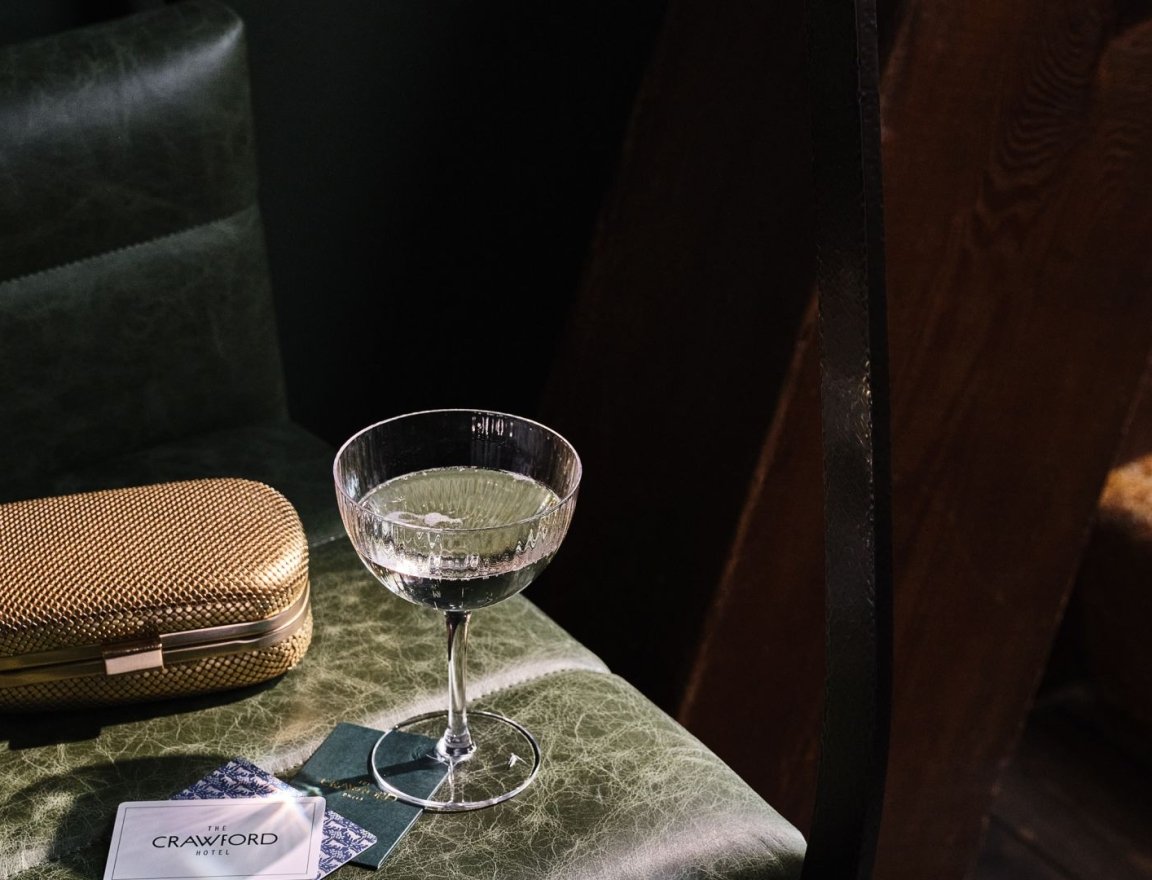 A martini glass on a table with a gold clutch purse.