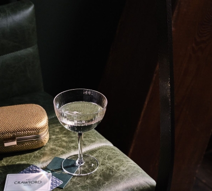 A martini glass on a table with a gold clutch purse.