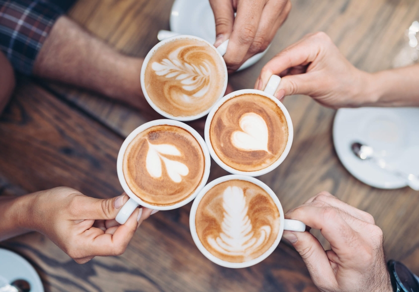 Four people clinking lattes. The lattes have decorative latte art.