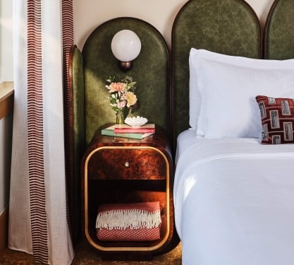 The bedside area of the Deluxe Classic Guest room at the Crawford Hotel in Denver, Colorado. The area has a small table with an extra blanket, fresh cut flowers and a lamp.