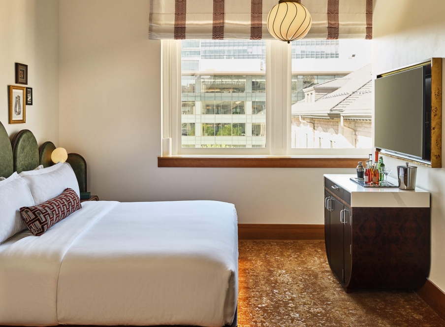 A king bed, bar cart and television in the Superior Classic Guest room at the Crawford Hotel in Denver, Colorado.