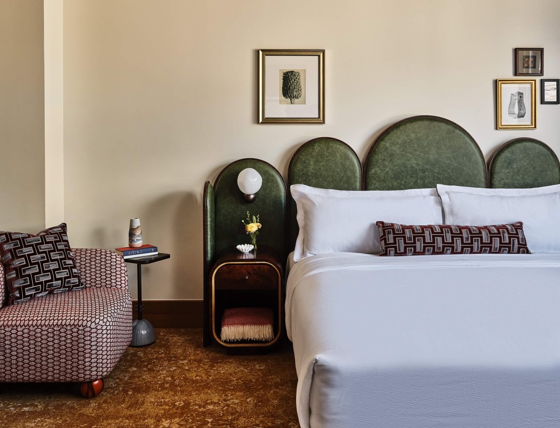 A king bed, chair, side table with fresh cut flowers and extra blanket in the Superior Classic Guest room at the Crawford Hotel in Denver, Colorado.