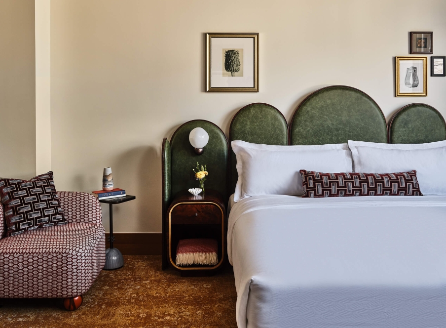 A king bed, chair, side table with fresh cut flowers and extra blanket in the Superior Classic Guest room at the Crawford Hotel in Denver, Colorado.