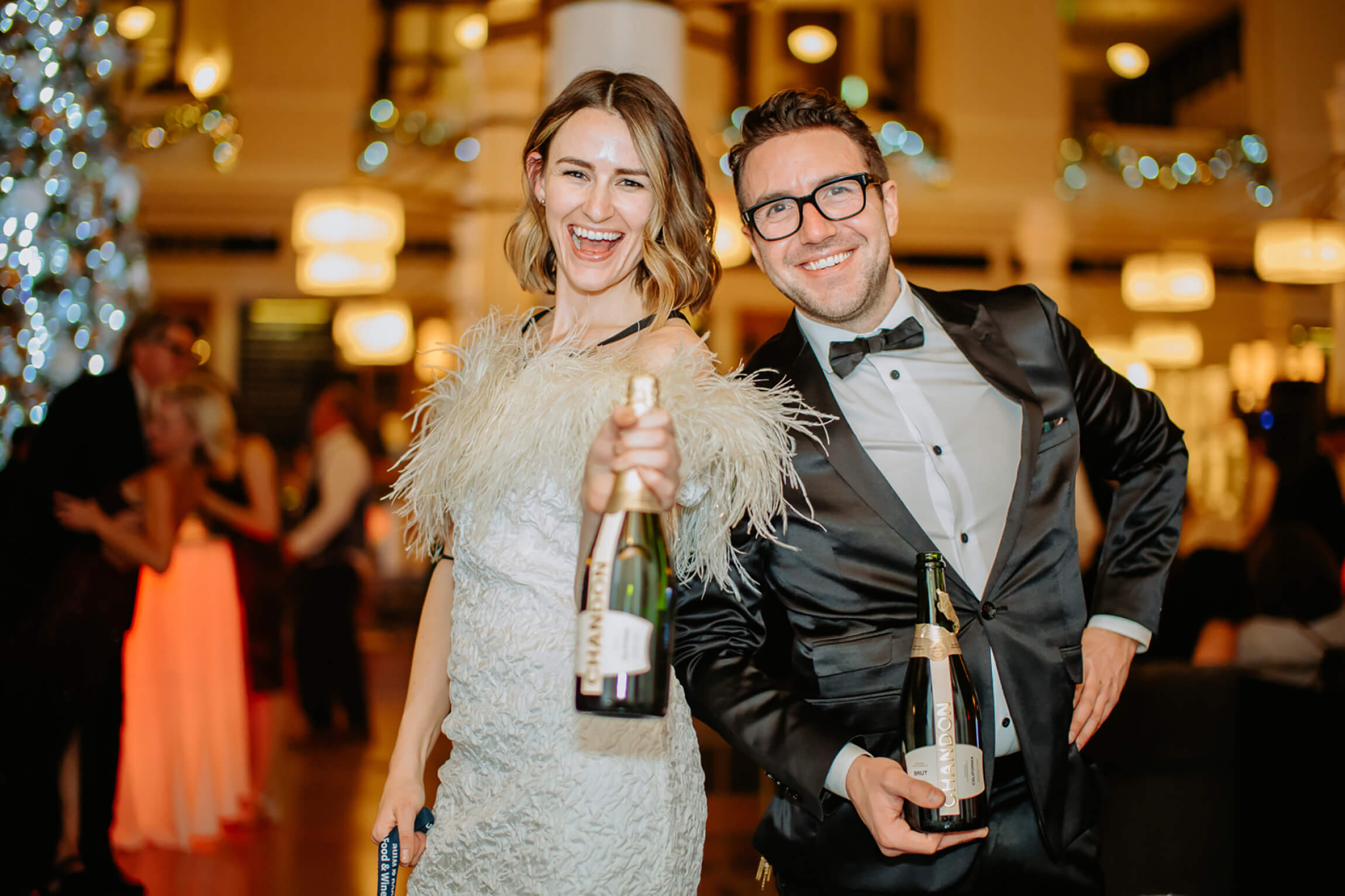 A bride and groom pose with champagne bottles at a wedding.