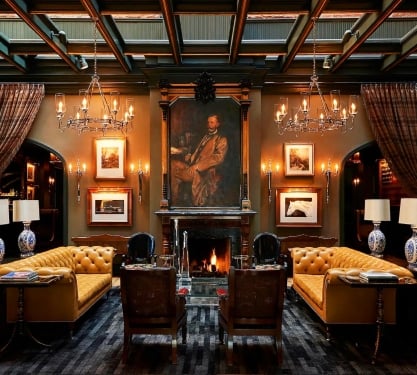 An opulent drawing room with a fireplace, leather furniture, and dark wood accents.