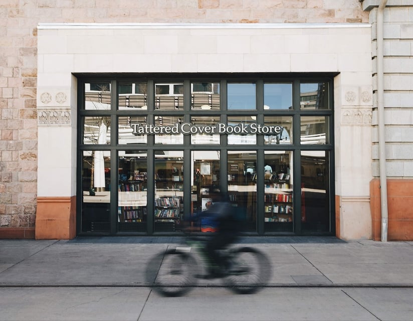 The exterior of Tattered Cover Book Store in Denver, Colorado. A cyclists goes by in a blur.