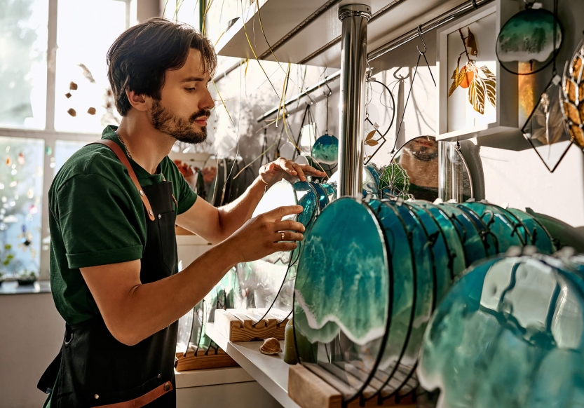 A shop owner adjusts a display of stained glass art pieces.