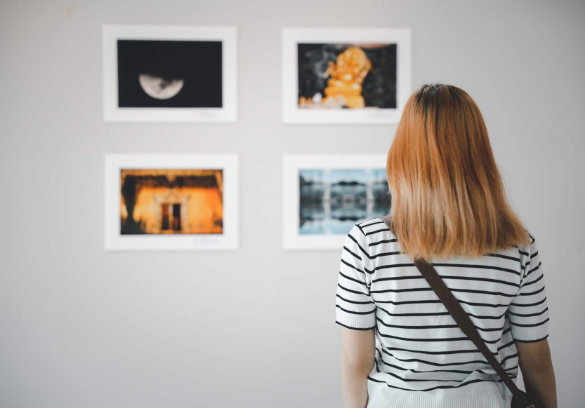 A woman with a striped shirt and mid-length hair looking at photographs on an art gallery wall.