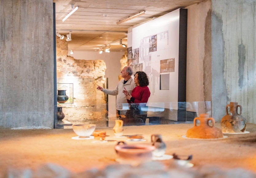 A museum exhibit of ancient pottery. A middle-aged couple stands in the background conversing.