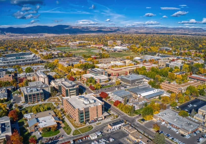 An arial view of Fort Collins, multi-use buildings in the foreground leading into woodland with a mountain range in the background.